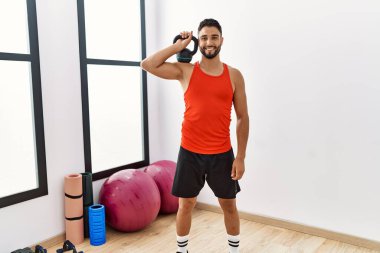 Genç Arap adam gülümsüyor spor merkezinde kettlebell ile antrenman yapıyor.