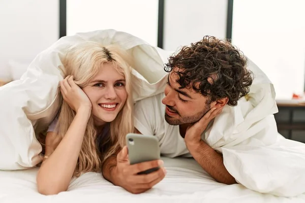 若いです美しいカップル使用してスマートフォン嘘自宅でベッド — ストック写真
