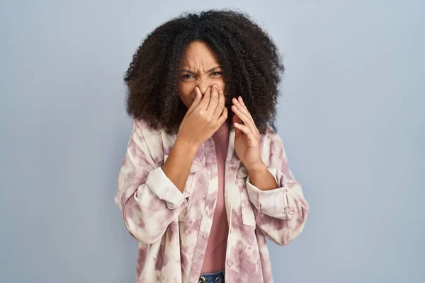 年轻的非洲裔美国女人站在蓝色的背景上 闻到一股难闻而恶心的气味 用手指捂住鼻子屏住呼吸 — 图库照片