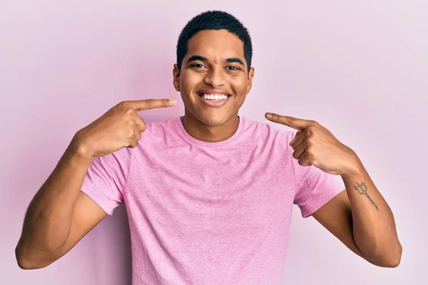 カジュアルなピンクのTシャツを着た若いハンサムなヒスパニック系の男性が陽気な表情と指の歯と口で指して笑っています 歯の健康の概念 — ストック写真