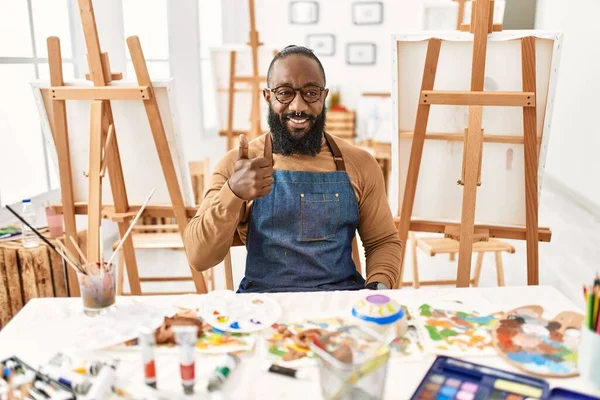 Sanat stüdyosundaki Afrikalı Amerikalı sanatçı elleriyle mutlu bir jest yapıyor. Kameraya bakıp başarıyı gösteren ifade. 