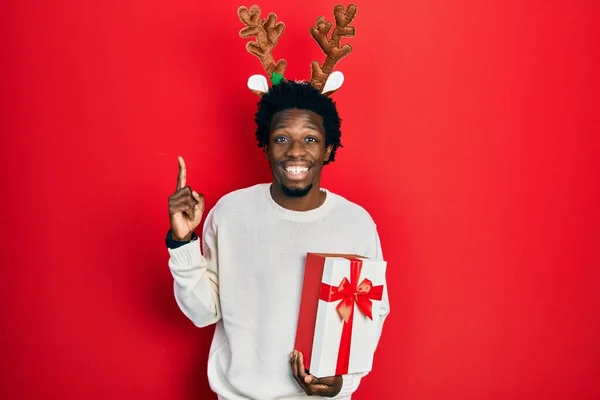 Mladý Africký Američan Nosí Jelení Vánoční Klobouk Drží Dárek Úsměvem — Stock fotografie