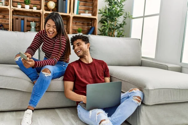 年轻的拉丁夫妇在家里用笔记本电脑和智能手机开心地笑着 — 图库照片