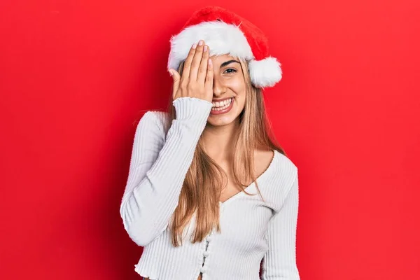 美丽的他的惊慌失措的女人 戴着圣诞帽 一只眼睛蒙着 脸上挂着自信的微笑 还有令人惊讶的情绪 — 图库照片