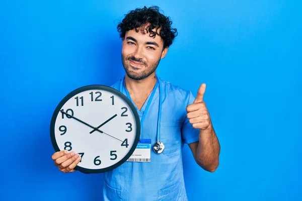 Молодой Латиноамериканец Синей Форме Медсестры Держит Часы Счастливыми Позитивными Большой — стоковое фото