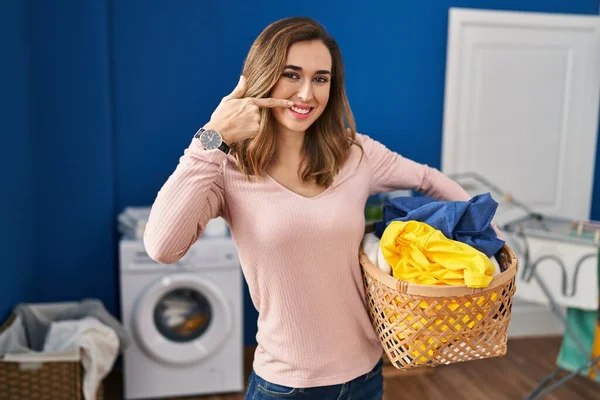 Ung Kvinna Håller Tvättkorg Pekar Med Handen Finger Mot Ansikte — Stockfoto