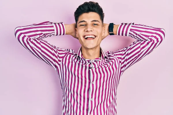 Young hispanic man wearing casual clothes relaxing and stretching, arms and hands behind head and neck smiling happy