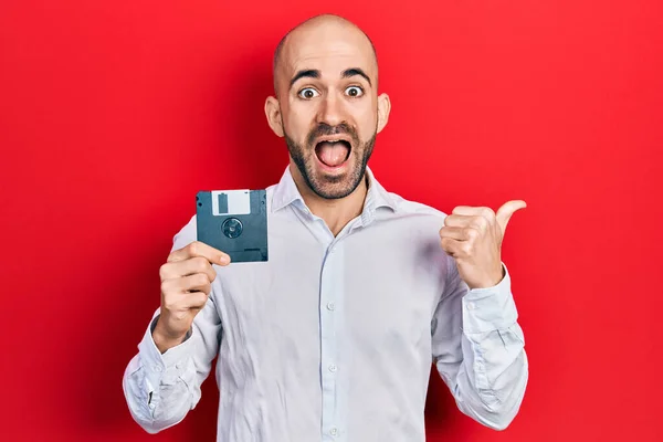 Joven Hombre Calvo Sosteniendo Disquete Apuntando Pulgar Hacia Lado Sonriendo — Foto de Stock