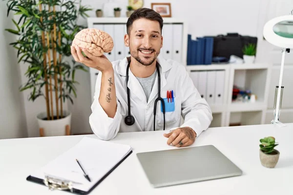 Młody Lekarz Trzymający Mózg Klinice Medycznej Wyglądający Pozytywnie Szczęśliwie Stojący — Zdjęcie stockowe