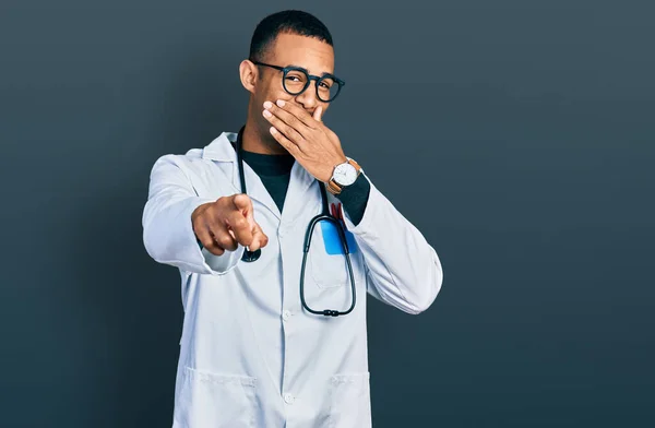 医師の制服を着た若いアフリカ系アメリカ人の男性と聴診器を身に着けて笑う 手でカメラを指差す口 恥の表情 — ストック写真