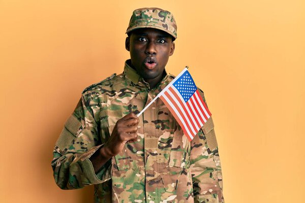 Young african american man wearing army uniform holding american flag scared and amazed with open mouth for surprise, disbelief face 