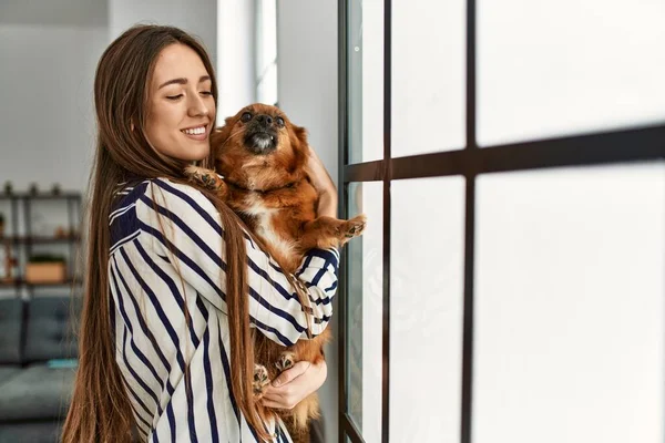 Joven Mujer Hispana Sonriendo Confiada Abrazando Perro Pie Casa — Foto de Stock