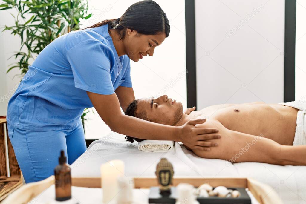 Young latin massage therapist woman giving relaxing treatment on man shoulders at beauty center.