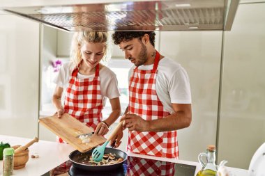 Genç çift mutfaktaki tavayı kullanarak mutlu bir yemek pişiriyor..