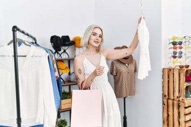 Genç beyaz kadın elbise mağazasından kendine güvenen bir şekilde gülümsüyor.