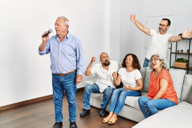 Bir grup orta yaşlı arkadaş evde mikrofon kullanarak şarkı söylüyor..