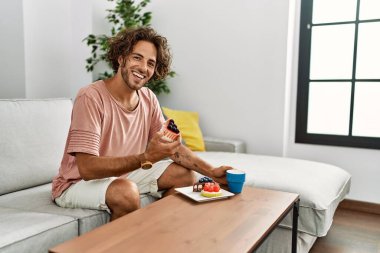 Genç İspanyol adam kahvaltısını yapıyor. Evdeki kanepede oturuyor..