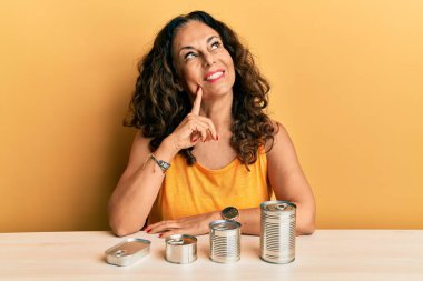Güzel orta yaşlı kadın, konserve yiyecekle ciddi bir yüz ifadesi, eli çenesinde soru sormayı düşünen, kafa karıştırıcı bir fikir hakkında düşünceli. 