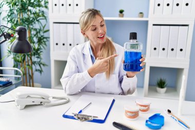 Dişçi üniforması giyen genç sarışın kadın klinikte gargara tutuyor.