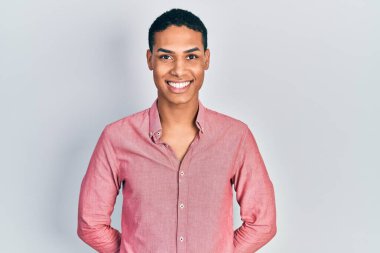 Genç Afro-Amerikan adam günlük kıyafetler giyiyor. Pozitif ve mutlu görünüyor. Kendine güvenen bir gülümsemeyle dişlerini gösteriyor. 