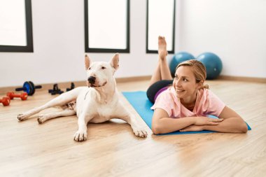 Beyazlı genç bir kadın spor merkezinde yoga minderine uzanmış kendinden emin bir şekilde gülümsüyor.