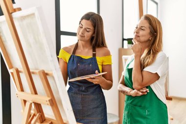 Anne ve kızı resim stüdyosunda kendine güvenen bir şekilde gülümsüyor.