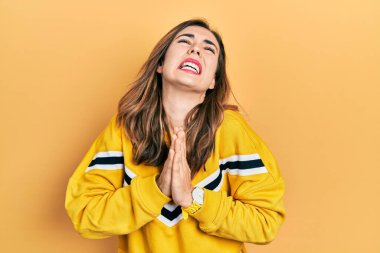 Gündelik giysiler giyen genç İspanyol kız elleri ile yalvarıyor ve dua ediyor. Yüzünde umut ifadesi var. Çok duygusal ve endişeli. Yalvarıyor. 