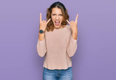 Güzel, beyaz bir kadın, gündelik kazak giyip çılgın bir ifadeyle bağırıyor ve elleri havada rock sembolü yapıyor. Müzik yıldızı. ağır müzik konsepti. 