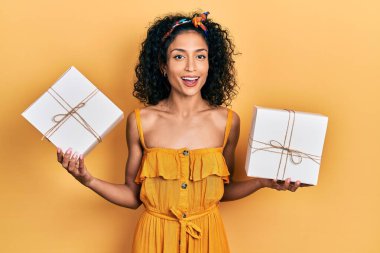 Genç Latin kız elinde hediyeler tutarak çılgınca kutlama yapıyor ve başarıya hayret ediyor gözleri açık heyecanla haykırıyor. 