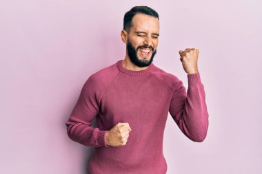 Sakallı, sıradan bir kazak giyen genç adam kolları havada ve gözleri kapalı bir şekilde başarıyı kutluyor ve şaşırıyor. 