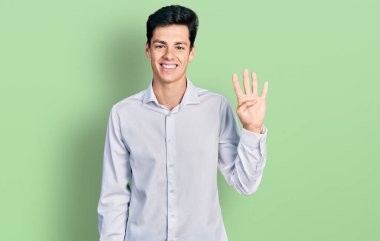 Genç İspanyol iş adamı iş kıyafetleri giyer ve parmaklarını dört numarayı göstererek gülümserken kendinden emin ve mutlu. 