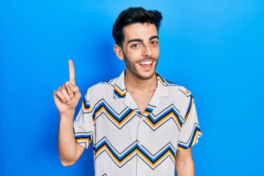 Gündelik kıyafetler giyen genç İspanyol adam başarılı bir fikirle işaret ediyor. Heyecanlı ve mutlu. Bir numara.. 
