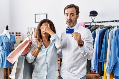 İspanyol orta yaşlı çift ellerinde alışveriş torbaları ve kredi kartı ile gözleri kapatıyorlar, ciddi ve üzgün görünüyorlar. Görme, saklama ve reddetme konsepti 