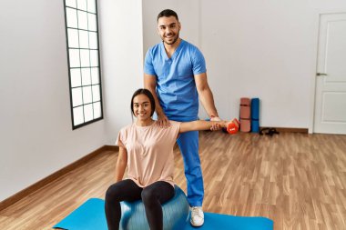 Latin erkek ve kadın fizyoterapist üniforması giyiyorlar rehabilitasyon merkezinde uygun top ve halterle rehabilitasyon seansı yapıyorlar.