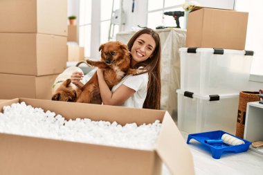 Genç İspanyol kadın gülümsüyor. Kendine güvenen, kucaklayan köpek yeni evinde yerde oturuyor.