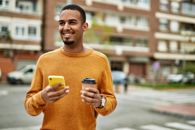 Genç Afrikalı Amerikalı adam akıllı telefon kullanıyor. Şehirde kahve içiyor..