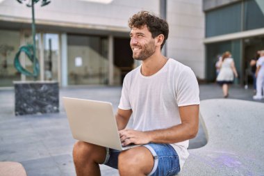 Sokakta dizüstü bilgisayar kullanarak gülümseyen İspanyol genç adam.