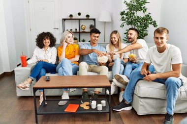 Mutlu bir şekilde gülümseyen bir grup genç arkadaş evde film izliyor..