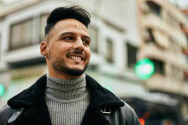Genç Arap adam gülümsüyor, mutlu bir şekilde şehirde duruyor..