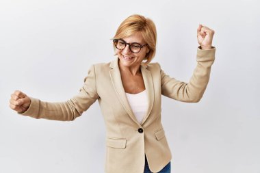 Orta yaşlı sarışın iş kadını izole edilmiş arka planda dans ediyor mutlu ve neşeli, gülümsüyor hareketli ve kendinden emin müzik dinliyor. 