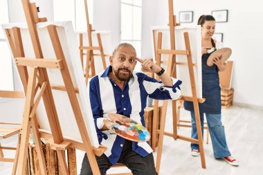 Sanat stüdyosundaki kıdemli sanatçı gülümseyerek tek parmağıyla kafasını işaret ediyor, harika bir fikir ya da düşünce, iyi bir hafıza. 