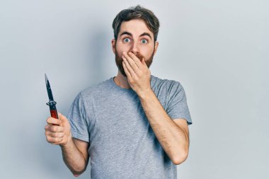 Sakallı, elinde çakısı olan beyaz bir adam ağzını eliyle kapatıyor, şok geçiriyor ve hata yapmaktan korkuyor. şaşırmış ifade 