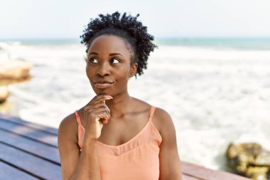 Genç Afro-Amerikan kadın, yaz kıyafetleri içinde sahilde dikilmiş ciddi bir yüz ifadesiyle el pençe divan duran, kafa karıştırıcı bir fikir hakkında düşünceli. 