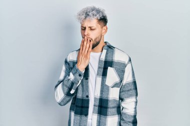 Modern boyalı saçlı, gündelik gömlek giyen, esnemekten sıkılmış, ağzı eliyle kapatan genç İspanyol bir adam. Huzursuz ve uykulu.. 