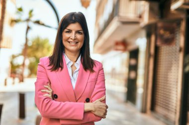 Güzel İspanyol iş kadını zarif bir ceket giyiyor. Şehre gülümsüyor, kolları kapalı.