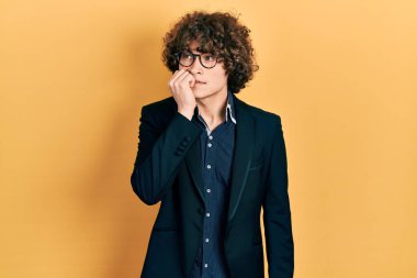 İş ceketi giyen, gözlüklü, stresli ve gergin görünen elleri ağızdan tırnak yiyen yakışıklı bir genç. anksiyete. 