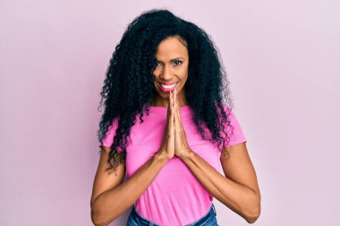 Orta yaşlı Afro-Amerikalı kadın gündelik giysiler giyip birlikte dua ederek af diliyor kendinden emin bir şekilde gülümseyerek.. 