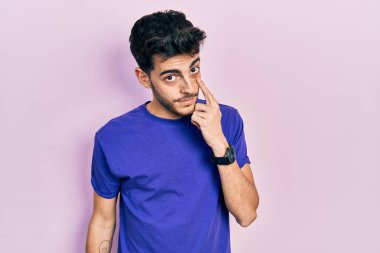 Gündelik tişört giyen genç İspanyol adam senin jestini ve şüpheli ifadeni izliyor. 