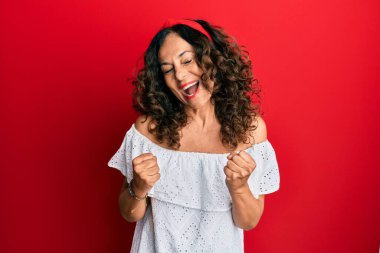 Orta yaşlı İspanyol kadın gündelik giysiler giyiyor başarı için heyecanlı kolları havada ve gözleri kapalı zaferi kutlarken gülümsüyor. Kazanan konsept. 