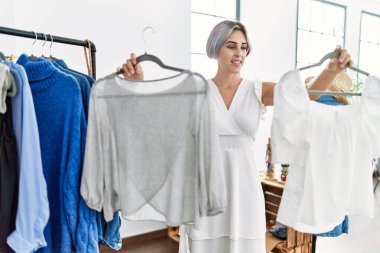 Genç beyaz kadın gülümseyerek giyim mağazasından kıyafet seçiyor..